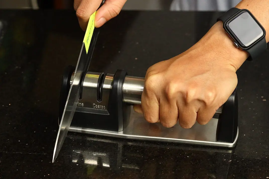 A hand holding the Priority Chef on a kitchen countertop and sharpening a knife with it.