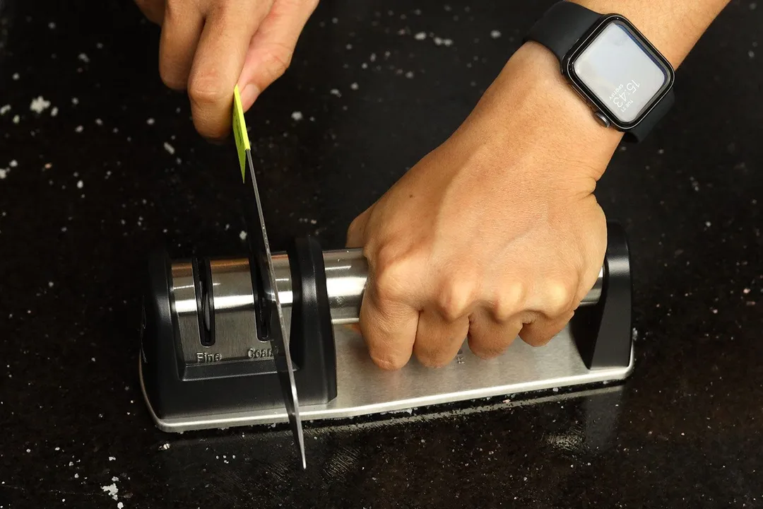 A kitchen knife being sharpened with the Priority Chef on a countertop sprinkled with salt particles