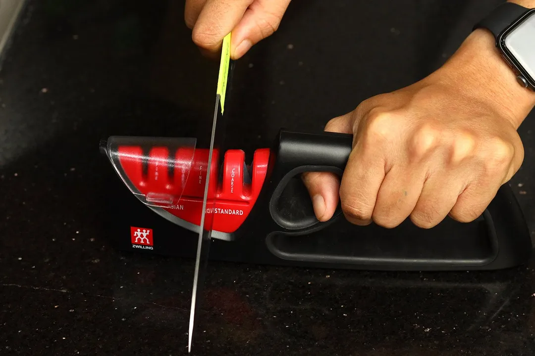 2 hands holding and sharpening a kitchen knife with the Zwilling knife sharpener on a countertop