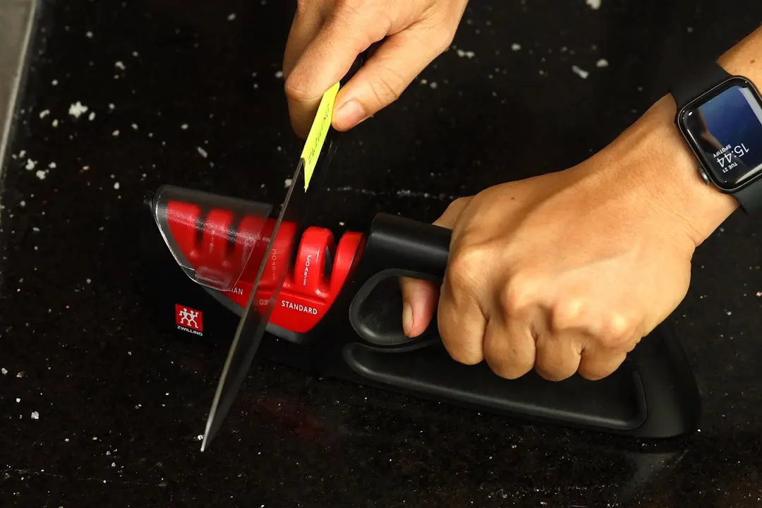 2 hands holding and sharpening a kitchen knife with the Zwilling 4-stage sharpener on a salt-sprinkled countertop