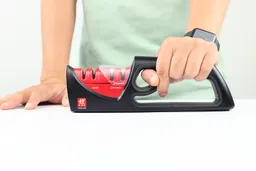 A hand holding the Zwilling knife sharpener and a hand resting on the table