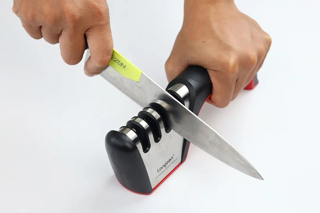 A kitchen knife being sharpened with the Longzon, and the 2 hands that hold the knife and the sharpener
