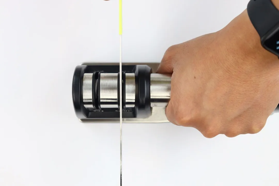 Top view of a kitchen knife being sharpened using the Priority Chef, which is held by a hand