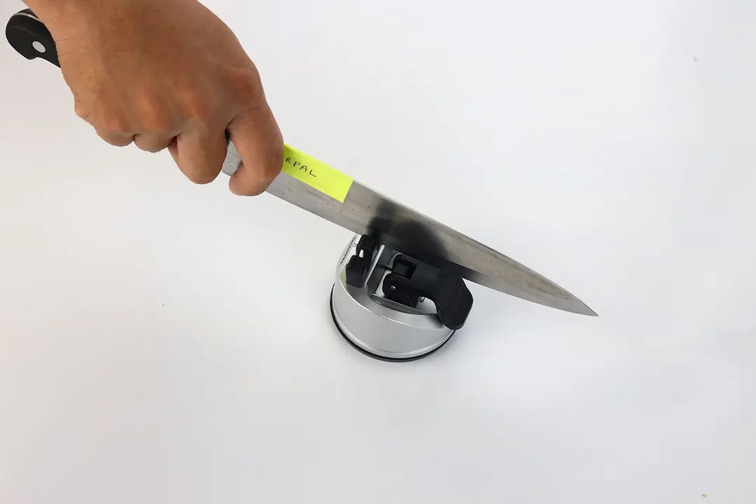 A hand holding and sharpening a kitchen knife with the Sharpal knife sharpener sharpener