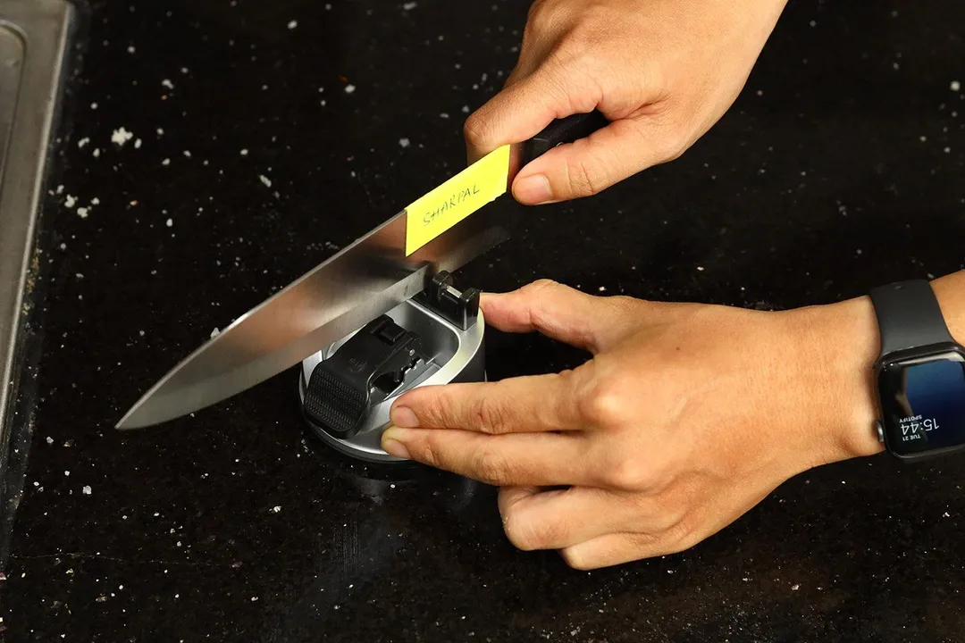 2 hands holding and sharpening a knife with the Sharpal knife sharpener on a salt-sprinkled countertop