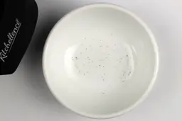 A bowl containing metal sharpening residue next to the base of the Kitchellence sharpener