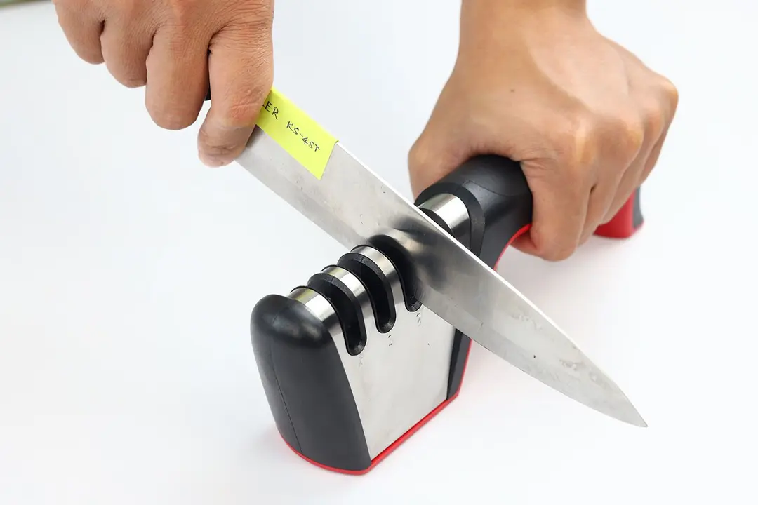 2 hands holding and sharpening a kitchen knife with the Mueller sharpener