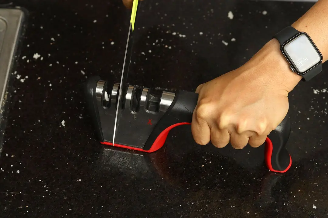 A kitchen knife being sharpened with the Mueller sharpener on a countertop sprinkled with salt particles