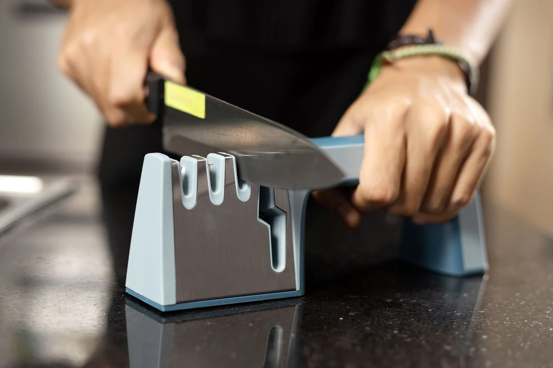 A person sharpening a knife with the Warmery sharpener on a countertop.