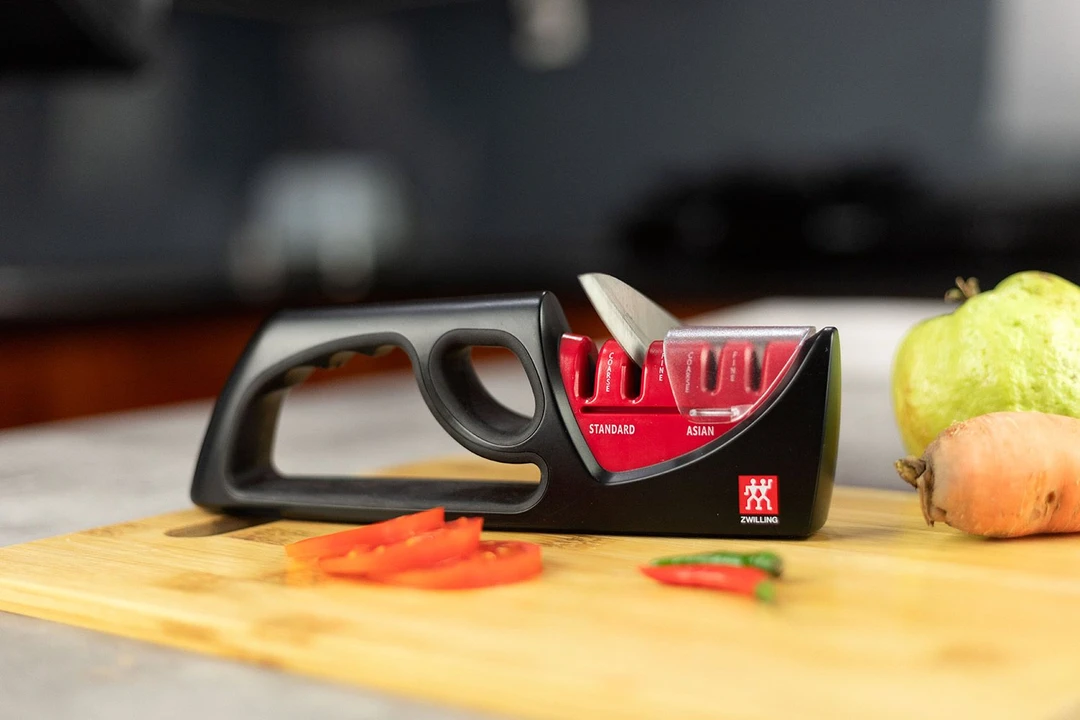 The Zwilling Henckels 4-Stage knife sharpener on a cutting board with chilli peppers, carrot, guava, tomato slices