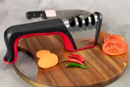 The Longzon 4-stage knife sharpener on a cutting board, kitchen knife, chilli peppers, carrot slices, tomato slices