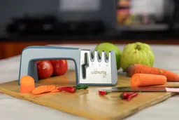 The Wamery 4-stage manual knife sharpener on cutting board with knife, carrots, carrot slices, tomatoes, chili peppers, guavas