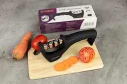 The Kitchellence 3-stage manual knife sharpener on cutting board, carrot, carrot slices, tomato, package box