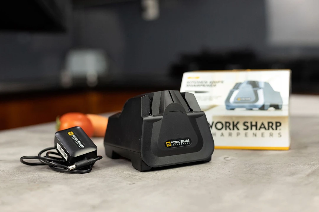 The Work Sharp CPE2 Electric Sharpener on countertop, its power cord, package box, tomato and carrot in background