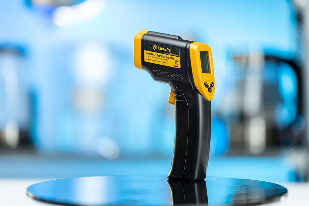 The Etekcity Lasergrip 1080 Infrared Thermometer standing upright on its handle on a turn table against a blurry blue backdrop.