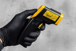 The black-gloved hand of a reviewer holding and using the trigger of the Etekcity Lasergrip 1080 IR thermometer.