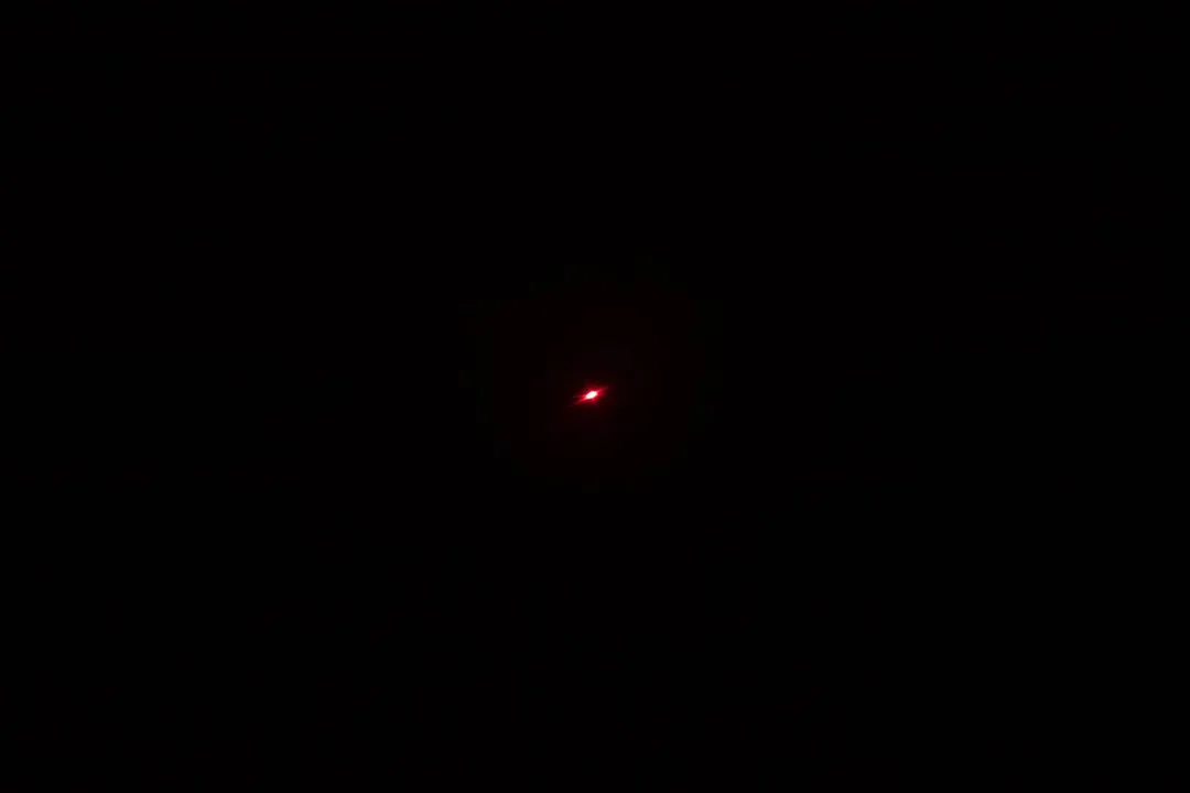 The red laser dot of the laser emitter on the Etekcity Lasergrip 1080 in a dark room.