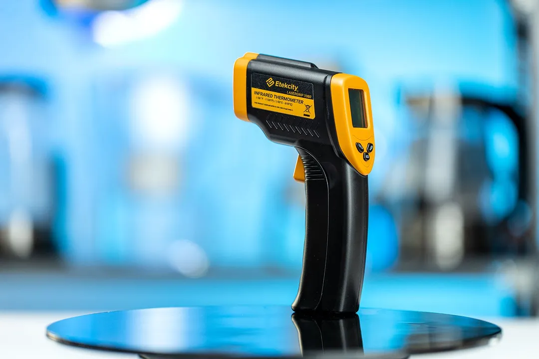 The Etekcity Lasergrip 800 Infrared Thermometer standing upright on a black turn table against a blurry, blue background.