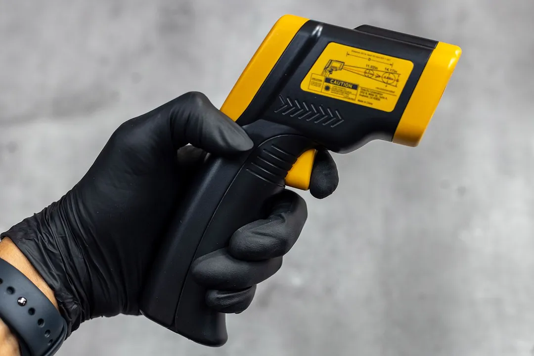 The black-gloved hand of a reviewer is pressing on the trigger of the Etekcity Lasergrip 800 IR thermometer.