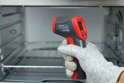 The gloved hand of a reviewer holding the Eventek ET312 IR thermometer. In the background is a toaster oven.