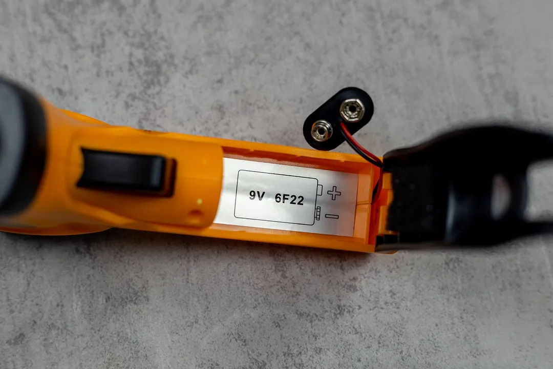 A view into the open battery compartment of the Helect IR thermometer. Inside is a label with the print “9V 6F22.”