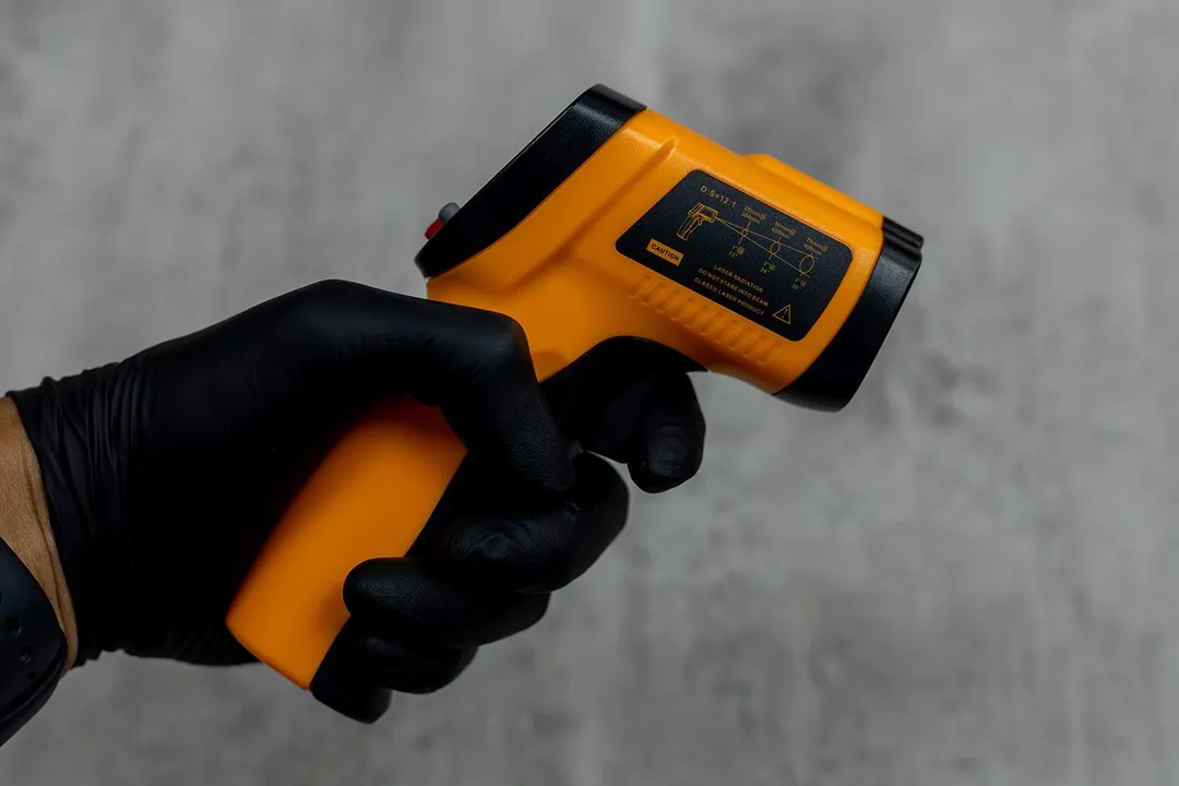 The Helect IR thermometer in the black-gloved hand of a reviewer.