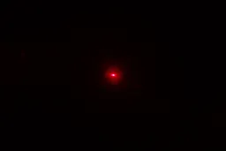 The red laser dot of the Helect IR thermometer gun’s laser emitter in a dark room.
