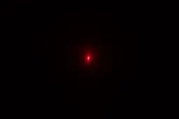 The red single-dot laser from the laser emitter of the Kizen LaserPro LP300 on the wall of a dark room.