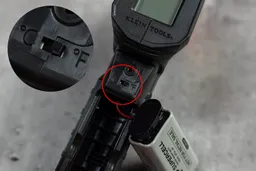 The screwed-in battery compartment of the Klein Tools IR1 thermometer is opened, revealing the receptacle for the 9V battery and a switch.