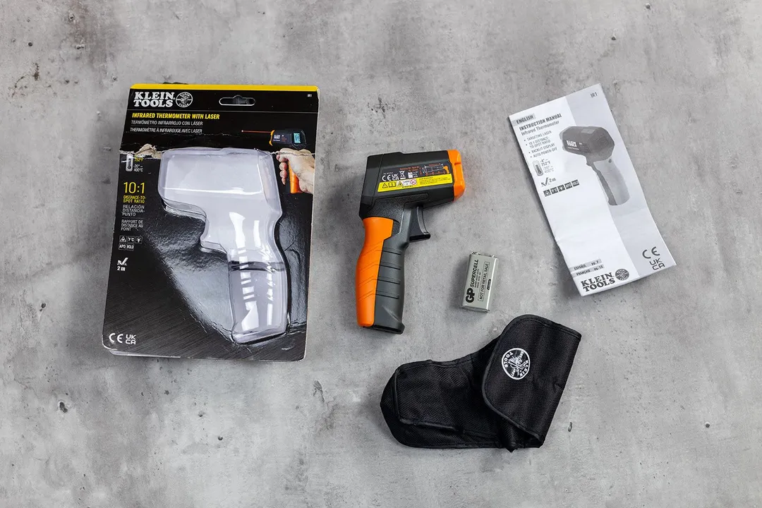 The Klein Tools IR1 is lying on its side in the center. To the left is the plastic packaging, to the right is the battery, the canvas holster, and user manual.