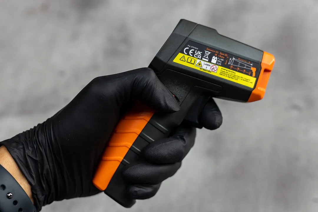 The black-gloved hand of a reviewer holding the Klein Tools IR1 IR thermometer.