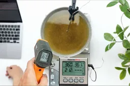 A reviewer is using the Klein Tools IR1 IR thermometer to measure the temperature of a hot pan of oil from 16 inches away. The screen displays 367°F.