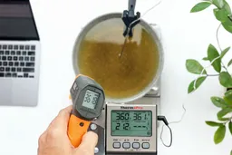 The Klein Tools IR1 is being used by a reviewer to measure the temperature of a hot pan of oil from 12 inches away. The screen shows 361.8°F.