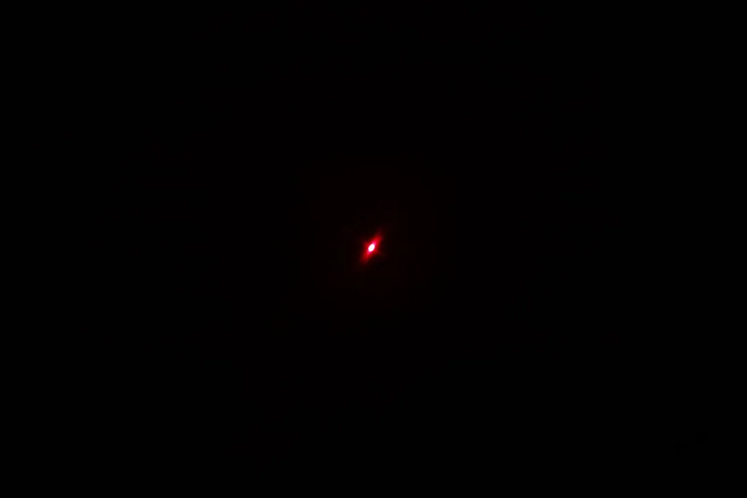 The red laser dot of the Klein Tools IR1 infrared thermometer gun’s laser emitter in a dark room.