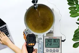 The Mecurate IRT600A is used to scan the temperature of boiling oil in a pan from 12 inches away. The screen reads 373°F.