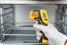 The gloved hand of a reviewer holding and using the Smart Sensor AS530 IR thermometer to measure the temperature of a toaster oven.