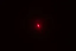 The bright red single-dot laser beam of the Sovarcate HS960D IR thermometer in a dark room.