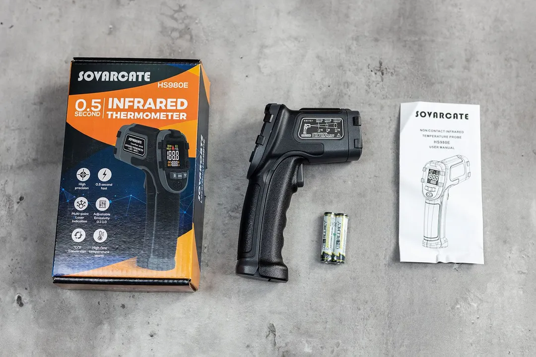 The Sovarcate HS980E IR thermometer is in the center. The shipping box is to the left, and the right are the batteries and the user manual.