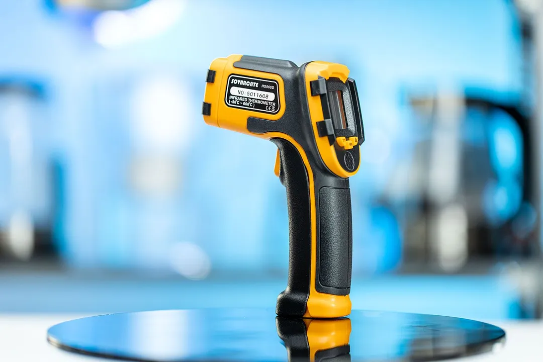 The SOVARCATE HS960D Infrared Thermometer standing upright on its handle on a turn table against a blurry blue backdrop.