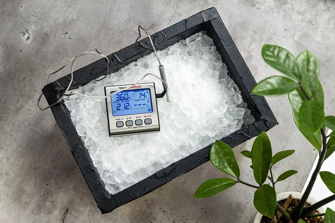 A temperature probe stuck to a thick layer of ice in an ice box, measuring its temperature. The screen displays 21°F.