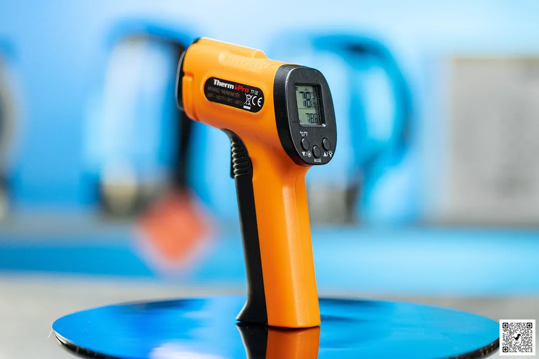 The ThermoPro TP-30 IR thermometer standing upright on a black turn table against a blurry blue background.