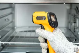 The ThermoPro TP-30 IR thermometer in the white-gloved hand of a reviewer, who’s using it to measure the internal temperature of a toaster oven.