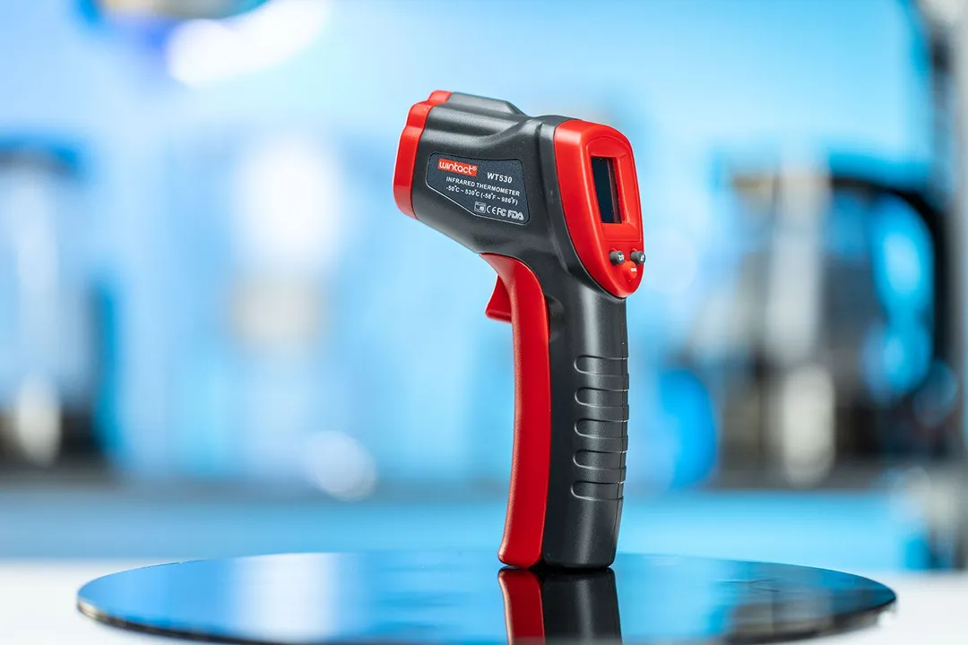 Wintact WT530 Infrared Thermometer standing upright on its handle on a turn table against a blurry blue backdrop.