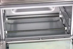 The cooking chamber ceiling of the Cuisinart TOA-60 Toaster Oven has two bottom nichrome heating elements. The cooking chamber has two guide rails with a safety hook on the left.