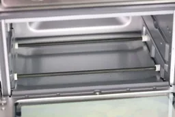 The cooking chamber ceiling of the Cuisinart TOA-60 Toaster Oven has two bottom nichrome heating elements. The cooking chamber has two guide rails with a safety hook on the left.