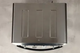 On a white background, the top of a closed stainless steel Cuisinart TOA-60 Convection Toaster Oven Air Fryer. In the front are the door handle and the control panel with four control knobs.