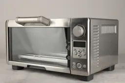 The front of a closed stainless steel Breville BOV450XL Mini Smart Toaster Oven has a control panel and the right has holes.