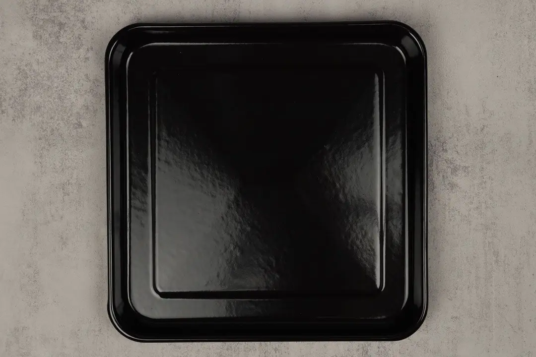 A enamel baking pan of the stainless steel Breville BOV450XL Mini Smart Toaster Oven on a grey background.