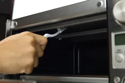 Brushing the upper heating element’s guards of the stainless steel Breville BOV450XL Mini Smart Toaster Oven’s glass door.
