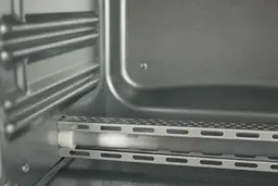 The bottom quartz heating element with guard and 2 guide rails on the left wall of the Comfee CFO-BB101’s cooking chamber.
